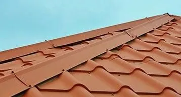 The image shows a red metal roof with neatly arranged corrugated panels, set against a clear blue sky.