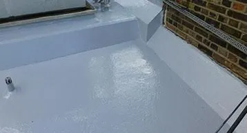 Flat roof section with a fresh coat of white waterproof sealing adjacent to a brick wall.