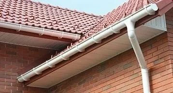 A brick house with red tile roofing and a white gutter system installed along the edge of the roof.