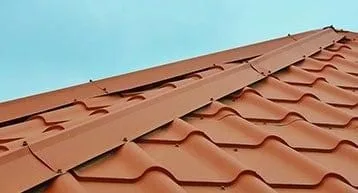 The image shows a red metal roof with neatly arranged corrugated panels, set against a clear blue sky.